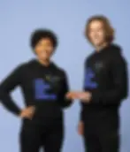 Two models wearing black Less Division More Connection hoodies with humanity design on a blue studio background