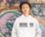 Man wearing a white hoodie with the message "Violence Breaks, Love Heals" standing in front of a colorful urban graffiti wall