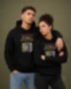 Couple wearing matching black unisex hoodies featuring the "Weapon Of Mass Deception" design.