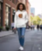 Woman wearing white Espresso Yourself unisex hoodie walking through the city with a coffee tumbler.