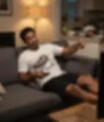 Man relaxing on couch watching TV, pointing toward someone else with amused expression while wearing white No.. You Do It slo