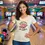 Thumbnail: Person in a natural scoop‑neck tee with a smiling pink donut and the pun “donut worry be happy” in a bright neon‑lit bowling