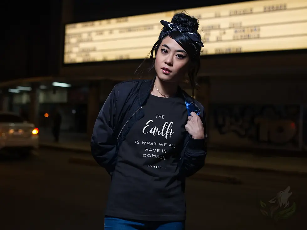 Black fitted tee with the Vegan Quotes “Earth in Common” design worn at night near a lit marquee.