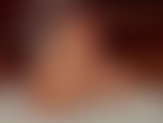 A medium close-up, side-profile photograph of a man with graying hair, resting his chin on his hand in a contemplative pose. He has fair skin and is wearing a light-colored, button-down shirt. The lighting is warm, and the background is softly blurred in shades of brown and dark red.