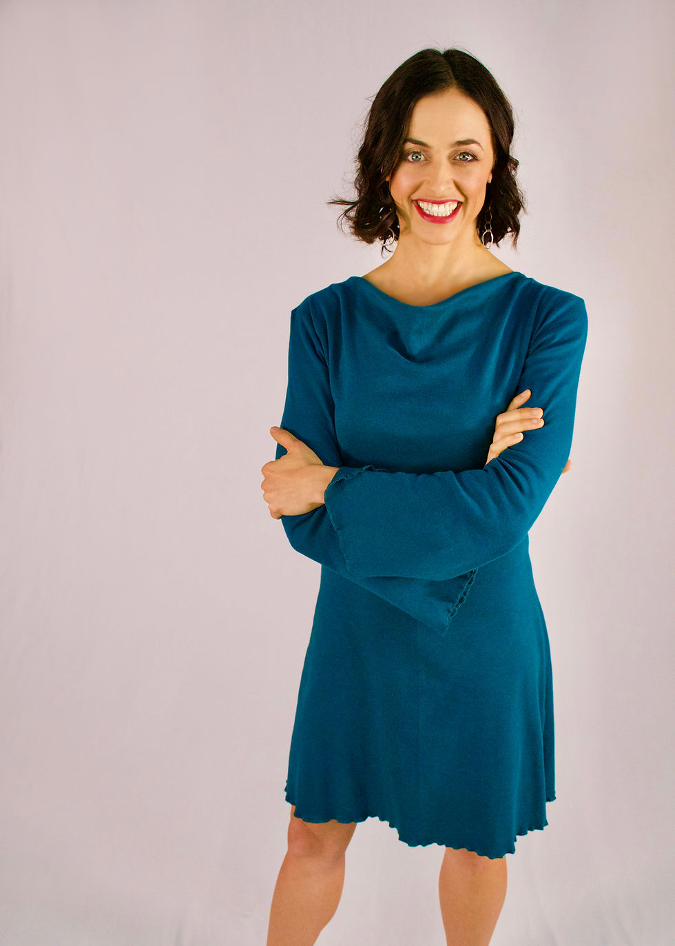 Dr. Suzannah Bozzone smiling with arms crossed, wearing a teal long-sleeved dress against a light background