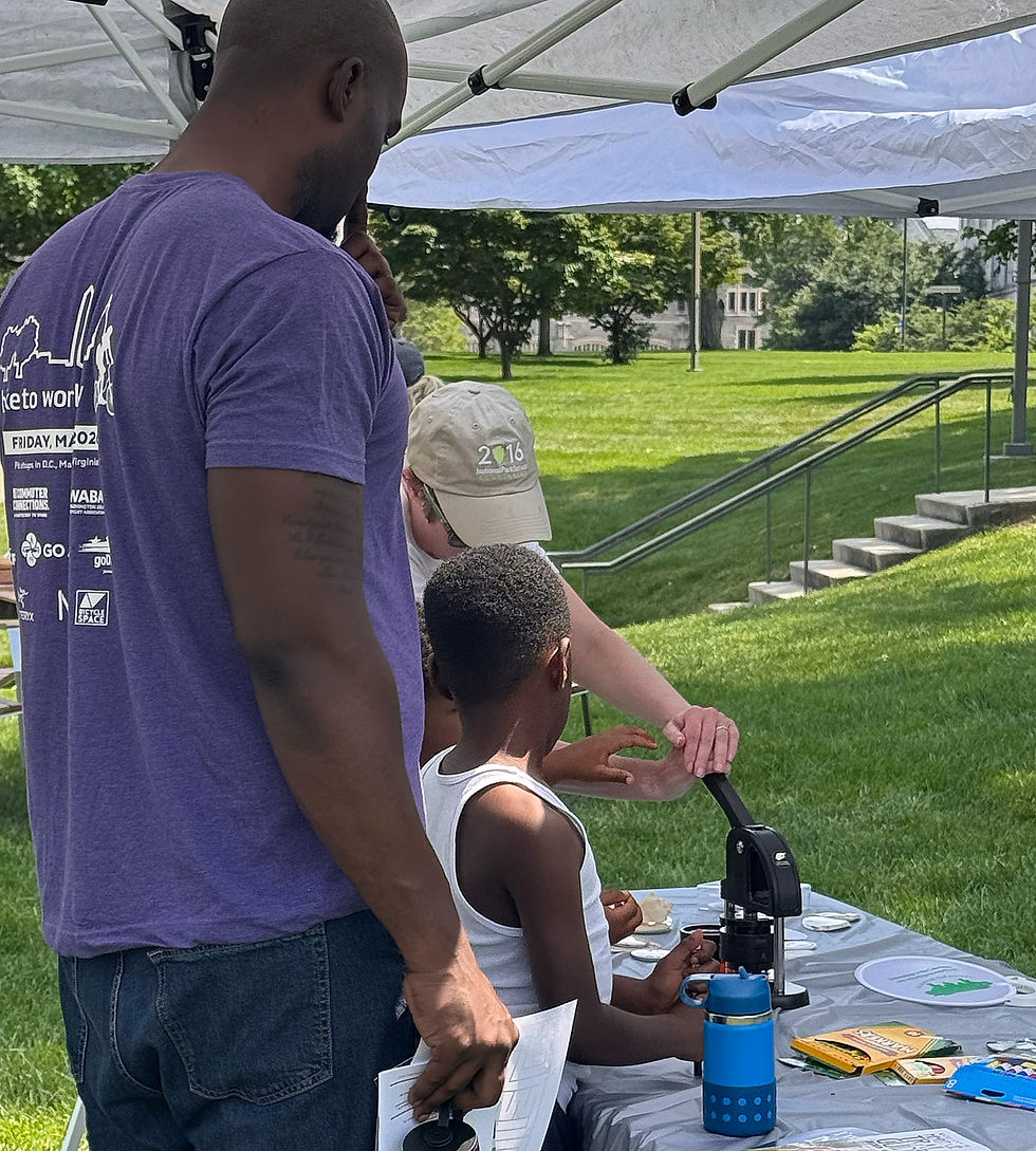 A child participates in a hands-on archaeology activity at an outdoor table while adults stand nearby under a canopy.