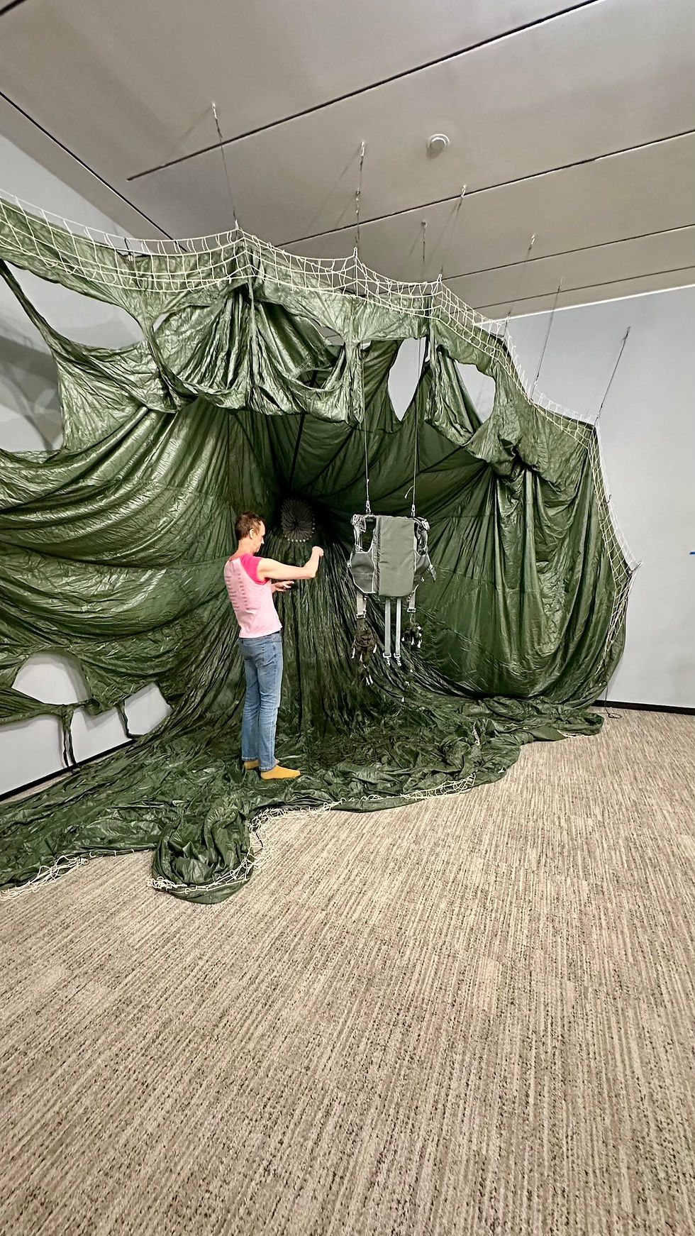 Paul Emmanuel standing with the suspended harness and parachute elements of Untethered/Retethered during installation at the Smithsonian.