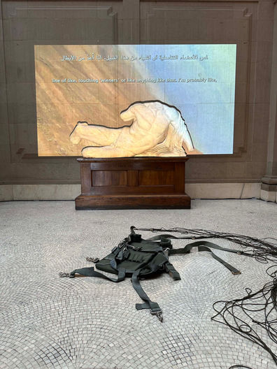 Installation view of ‘Untethered’ (2024) in the main court at Maryland Institute College of Art, Baltimore, MD, USA. Decommissioned, model T-10, U.S. military personnel parachute with severed suspension lines, detached harness with risers, 550 para-cord. High-definition video projection, stereo soundtrack, 7 min 26 sec. Parachute diameter: 35 feet. Harness dimensions: 30 x 30 inches (excluding suspension lines)