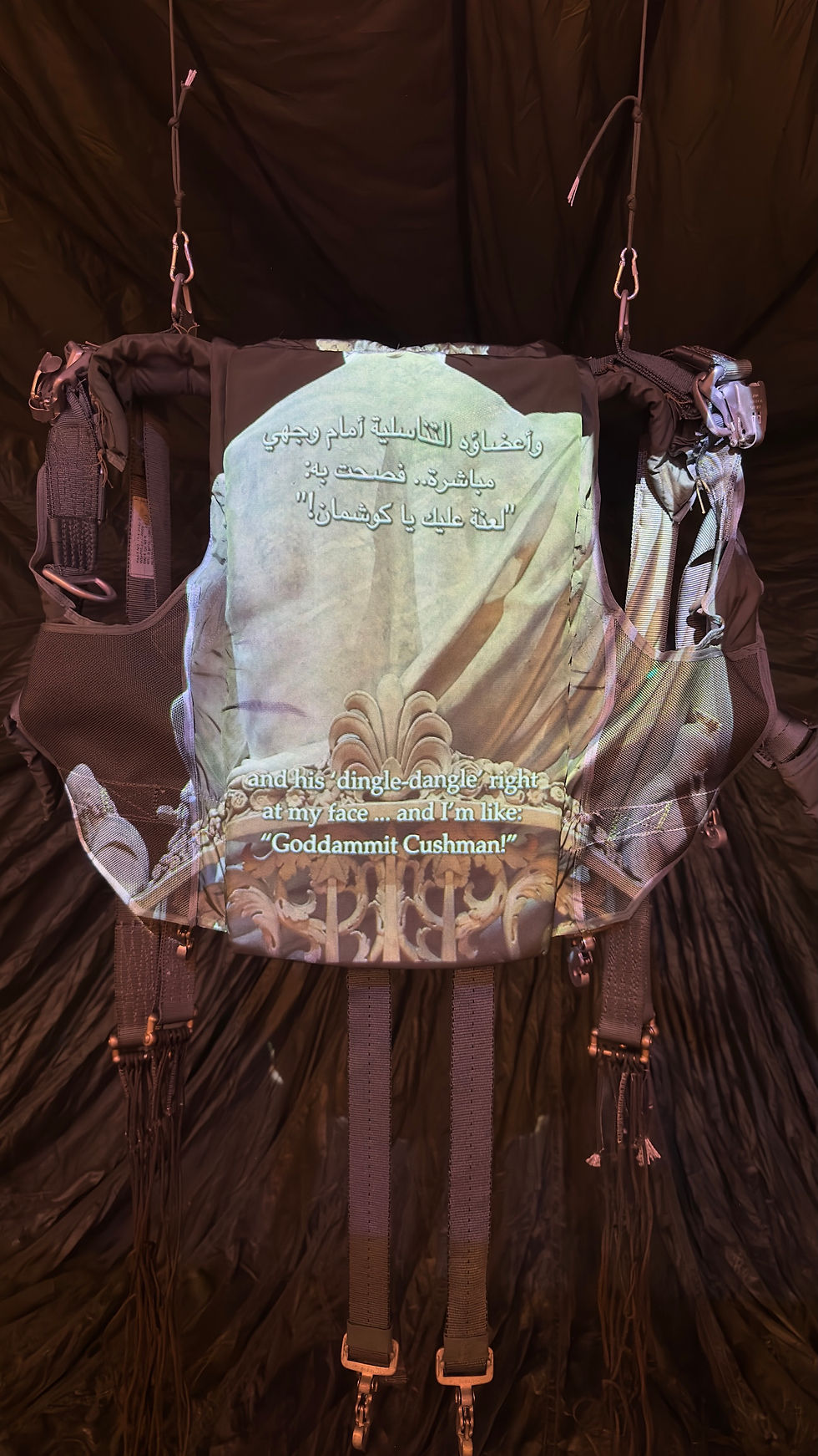 Video projection with Arabic and English text falling across the suspended military harness in Paul Emmanuel’s Untethered/Retethered.