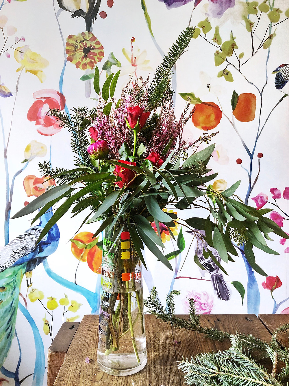 Peonies, roses and greenery in bouquet against floral wallpaper on wood table