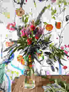 Peonies, roses and greenery in bouquet against floral wallpaper on wood table