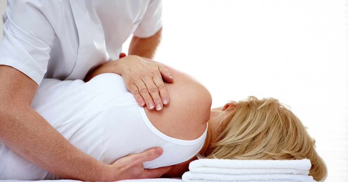 A chiropractor assessing a person's spinal movement before discussing treatment options in a clinical consultation.