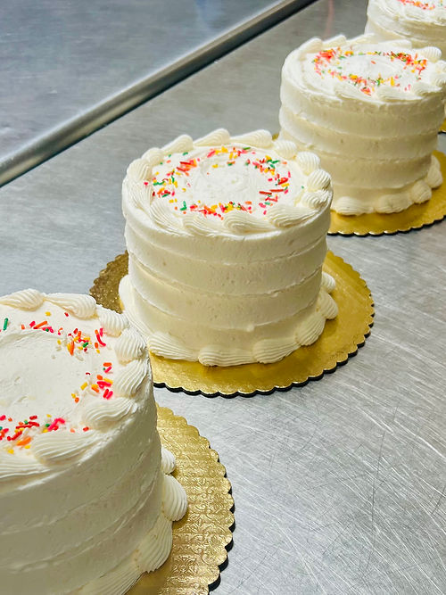 Three gluten-free funfetti cakes with vanilla cream frosting, piped borders, and colorful sprinkles, displayed on gold cake.