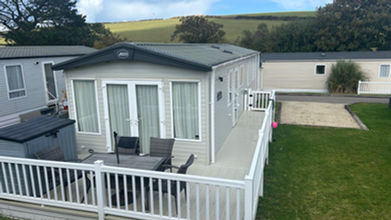 Holiday home with decking and furniture, located on a green lawn.