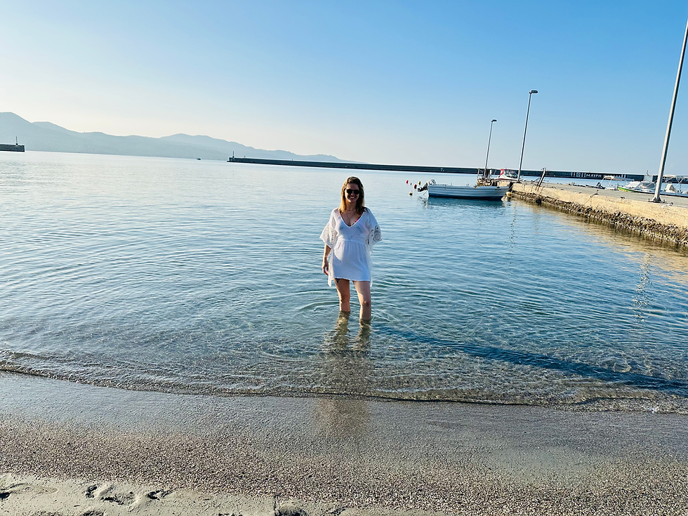 A traveler standing ankle-deep in the crystal-clear waters of Kalamata Town Beach, Greece
