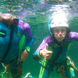 Un cliente che riemerge dall'acqua limpida del torrente con le braccia alzate e un grande sorriso dopo un tuffo nel canyon.
