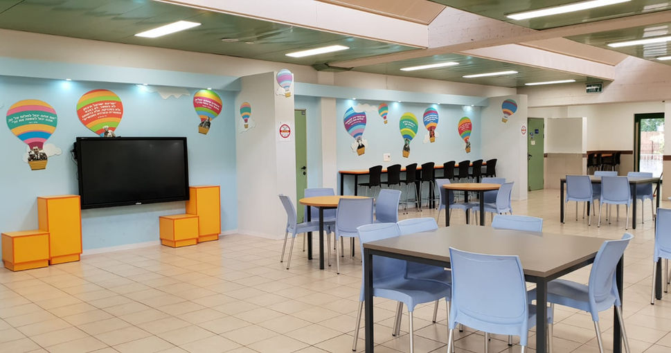 חדר אוכל בית ספר עם שולחנות וכיסאות, קישוטים של בלונים, מסך גדול