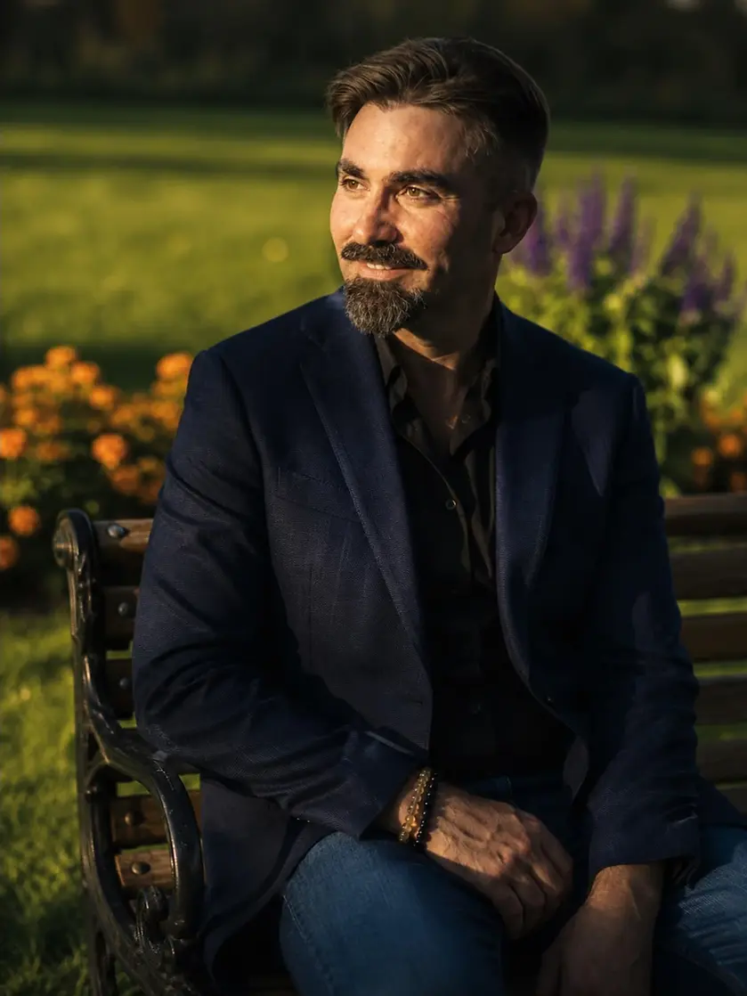Portrait d’Adriano Mourelle, coach et Maître Praticien en PNL à Lausanne, assis sur un banc dans un jardin.