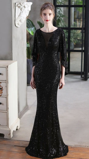 A model poses in a boutique, wearing the black Maggie sequin plunge neck maxi dress with long draped sleeves - perfect for special events or evening-wear.