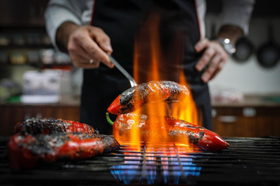 Open flame at a bbq, a male hand handleing a grilled sausage.