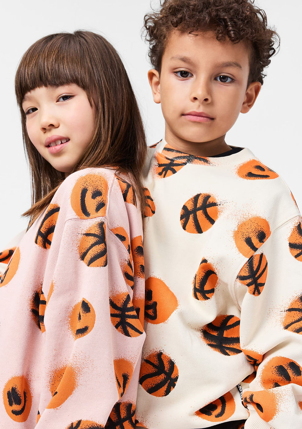 Two children standing side by side, wearing matching printed sweatshirts.