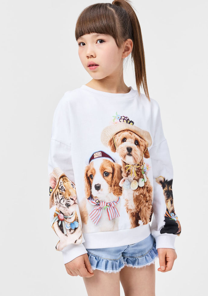 Child wearing a white sweatshirt with dog graphics, paired with denim shorts.