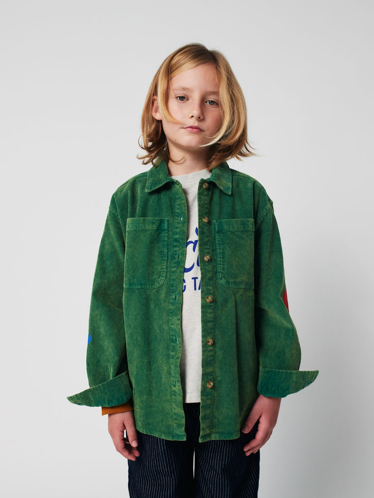 Side view of child leaning against wall while wearing green corduroy shirt