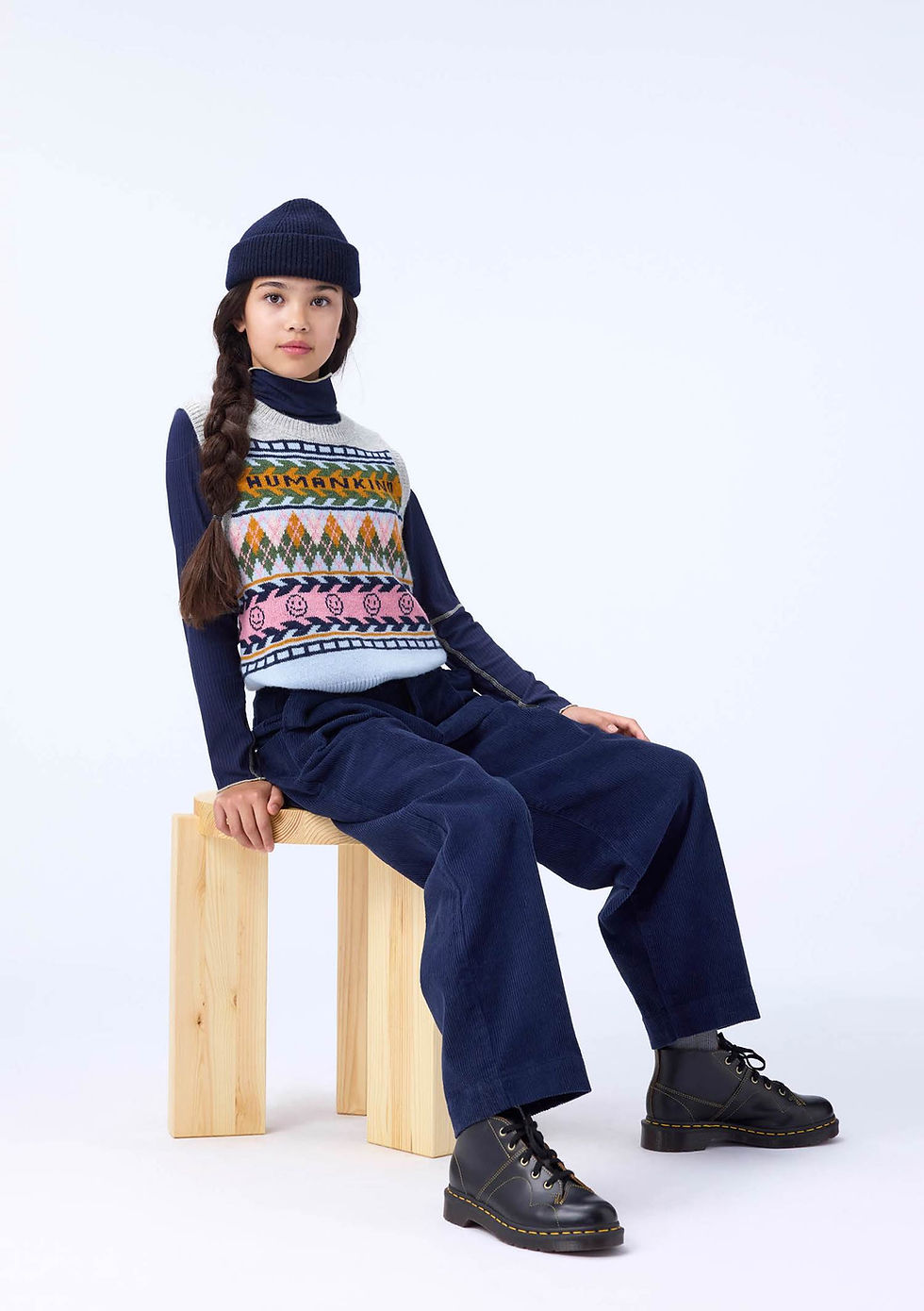 Girl wearing Molo Grace Kind Argyle vest sitting on a wooden stool