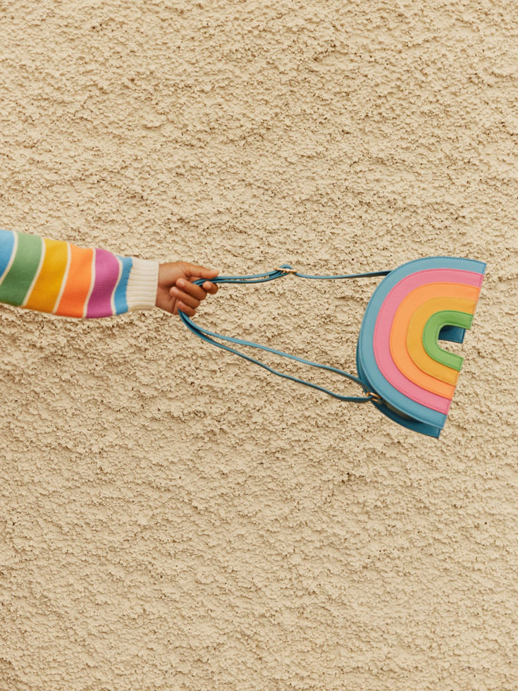 Close-up of a child holding the rainbow bag against a textured wall.