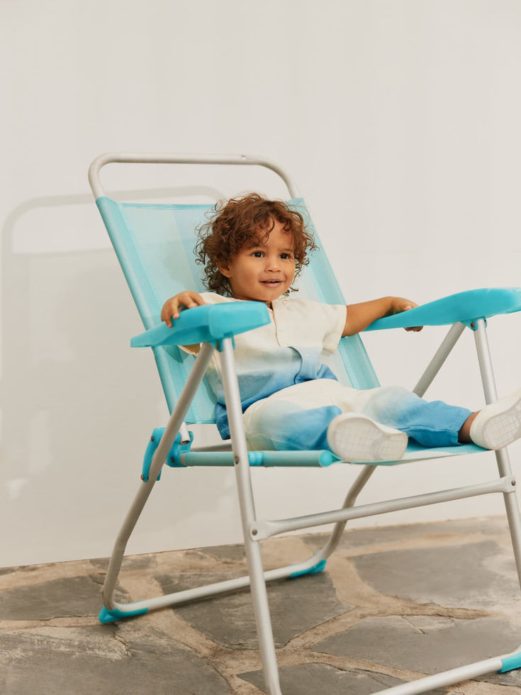 Child relaxing on a chair outdoors, wearing the gradient shirt.