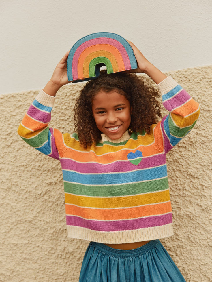 Child smiling and holding the rainbow bag above their head while wearing a striped sweater.