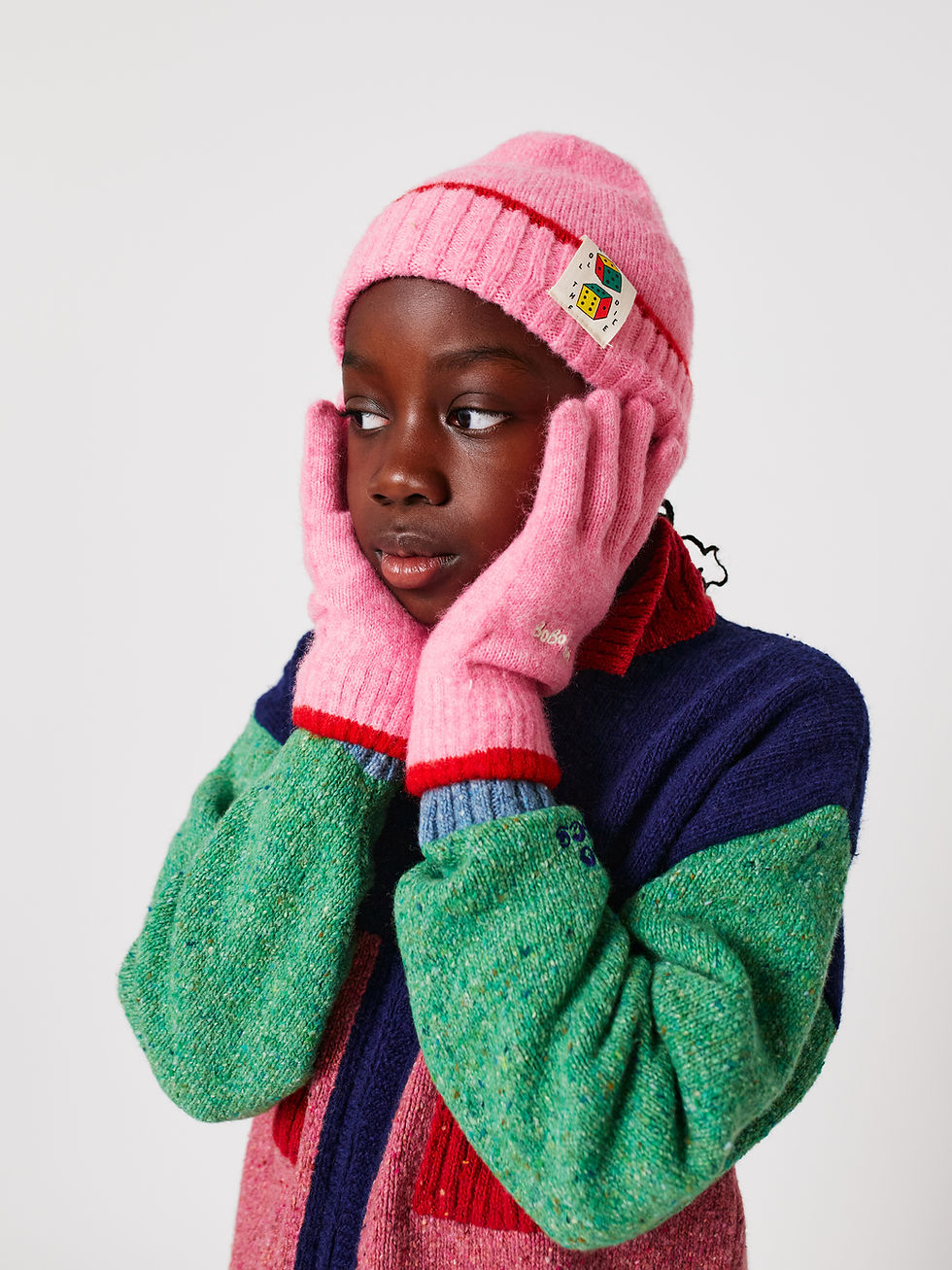 Child wearing pink gloves styled with matching beanie and color block sweater