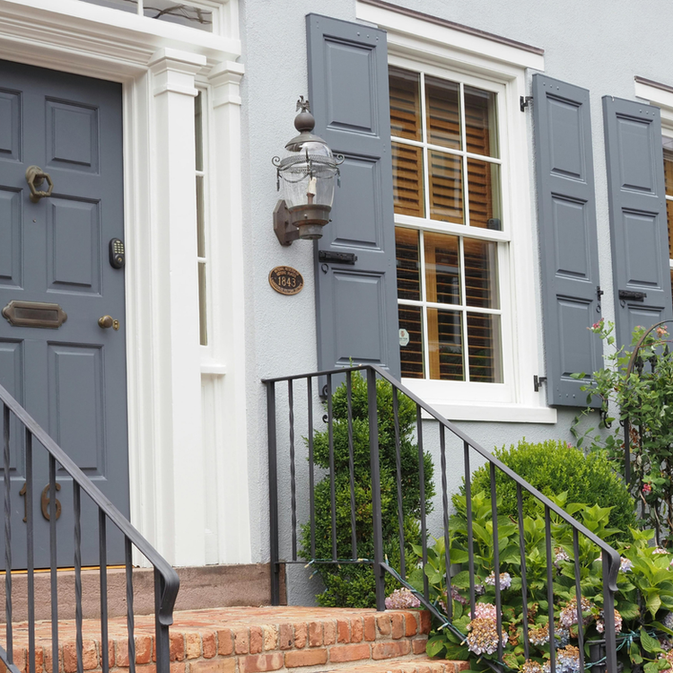 Gray door with address marker, windows, and shutters on a house facade
