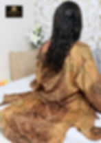 Mujer de espaldas con túnica dorada estampada en una cama.