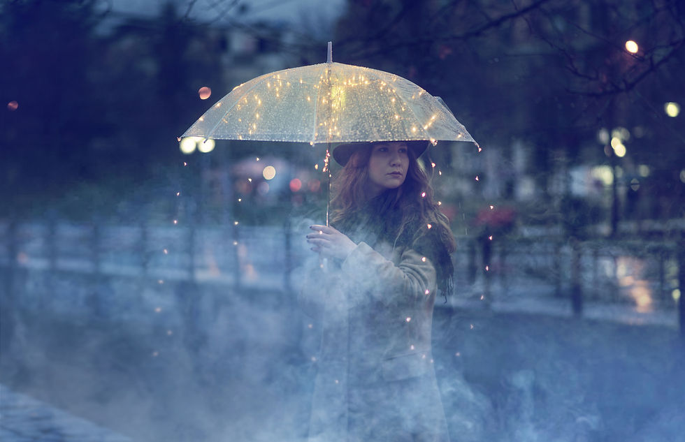 Woman in a hat holds an umbrella strung with fairy lights in a rainy, foggy city at dusk, looking pensive