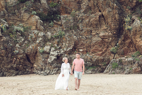 Laurine et Dorian marchant main dans la main sur une plage de sable devant une falaise rocheuse.