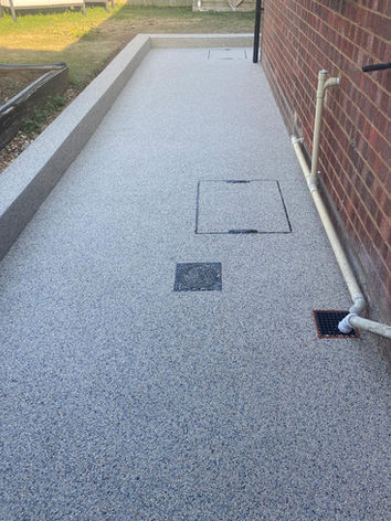 A professionally installed light grey resin-bound pathway in Huntingdon, Cambridgeshire, featuring a clean raised resin edge, integrated drainage and neatly finished access covers. Completed by Drayton Estates Group, Cambridgeshire Resin Specialists.