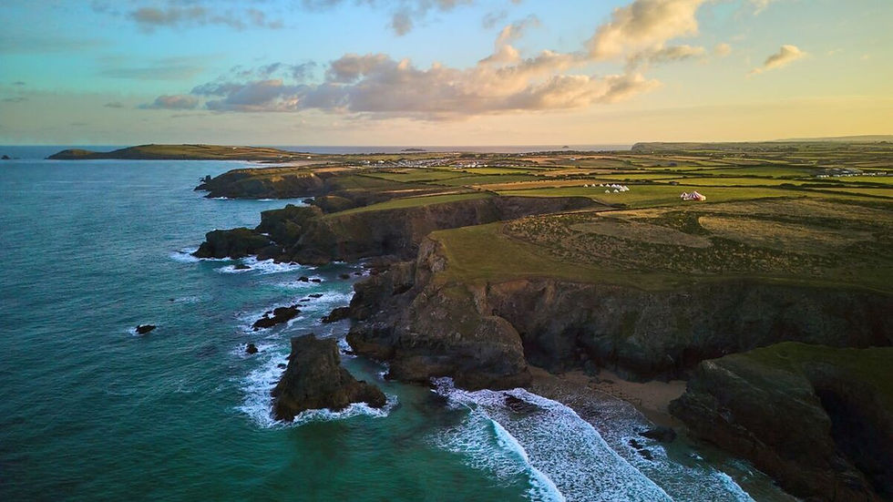 Imagem mostra uma paisagem com uma praia e na encosta ricanceiras com um verde tocado por um nascer do sol