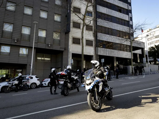 Policiais em motos e viaturas estacionados em frente a um prédio comercial, durante o dia.