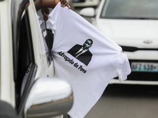 Pessoa segura camiseta para fora da janela do carro com a escrita "Advogado do Povo"