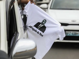 Pessoa segura camiseta para fora da janela do carro com a escrita "Advogado do Povo"