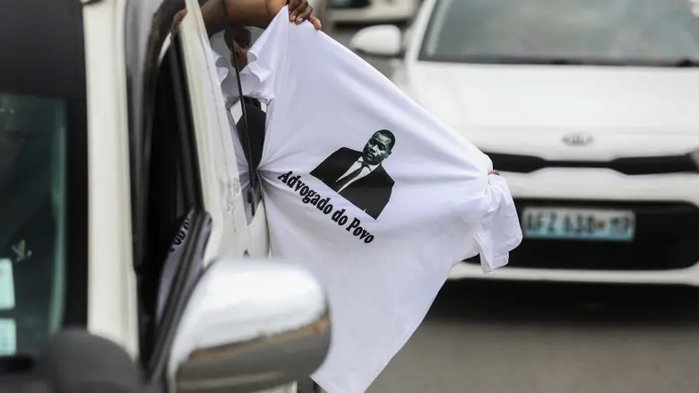 Pessoa segura camiseta para fora da janela do carro com a escrita "Advogado do Povo"