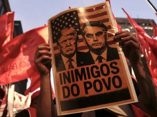 Protestante segura cartaz com imagens de Trump e Bolsonaro escrita 'Inimigos do Povo'