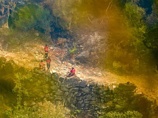 A imagem mostra bombeiros em um ambiente natural e rochoso, que parece ser uma área de trilha ou montanhismo