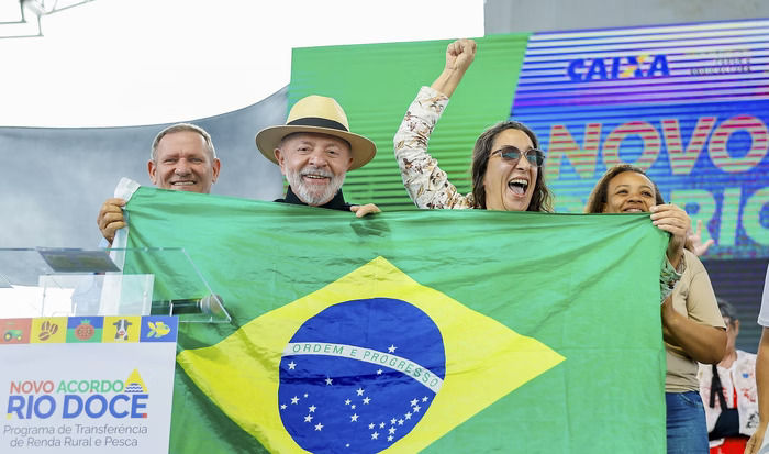 Lula segura bandeira do Brasil em mãos junto de mulher sorridente