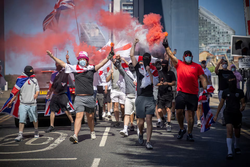 Ativistas mascarados com sinalizadores juntam-se aos manifestantes do grupo hoteleiro anti-asilo Pink Lady