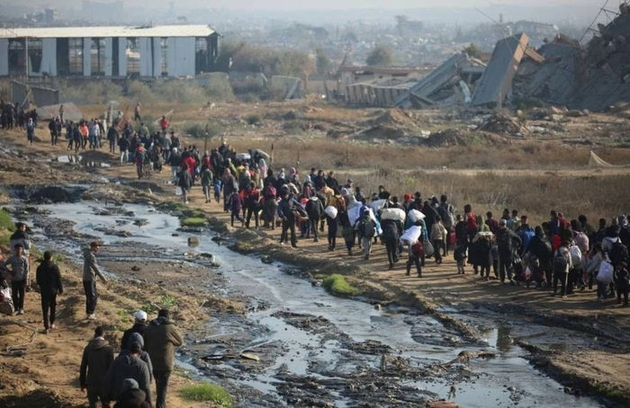 Pessoas carregando sacos e mochilas enfileiradas em gaza