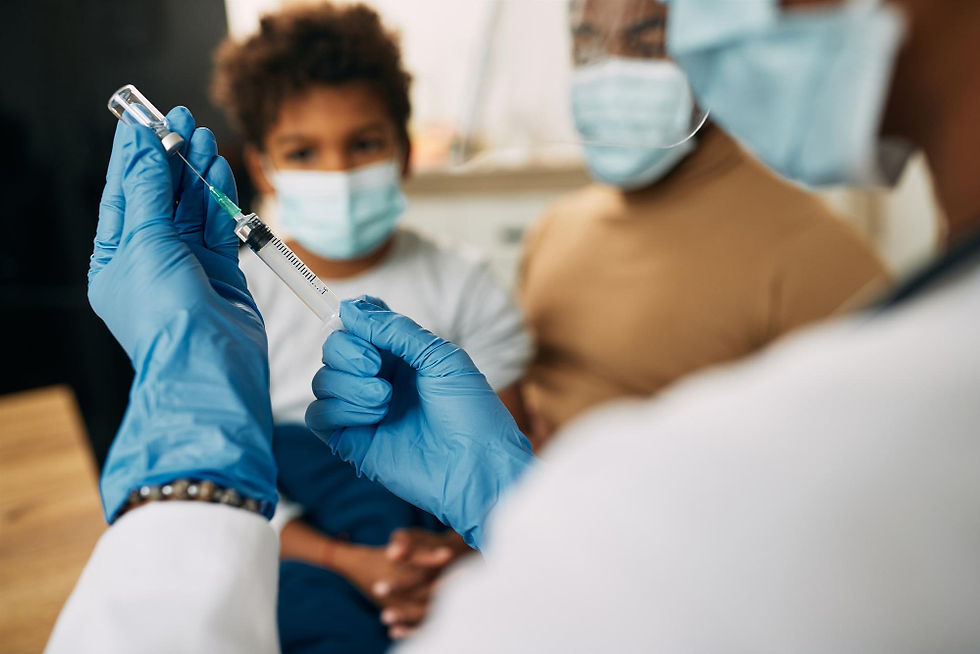 Profissional maneja vacina e ao fundo estão uma mãe e criança em seu colo esperando pela vacina