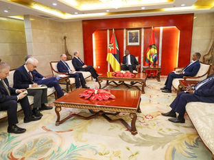 Reunião formal em uma sala de governo. O Presidente de Moçambique, Filipe Nyusi, está sentado ao centro, próximo a duas bandeiras moçambicanas. À sua frente, uma delegação italiana com vários homens de terno toma notas e acompanha a conversa.