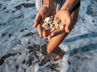 Mulher segura pequenas conchas na mão enquanto caminha na água do mar